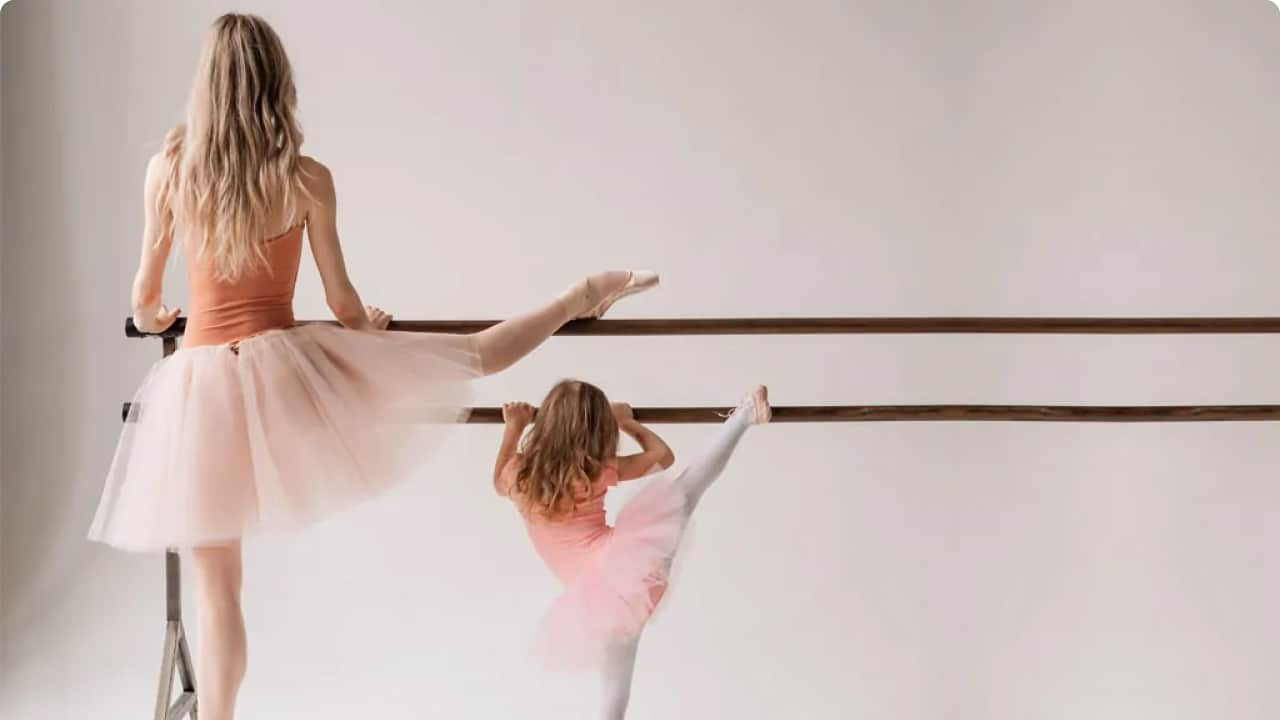 A young girl is guiding a little gymnast about gymnastic bar