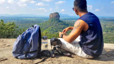 Man Sitting on Top of Gray Cliff Mountain Beside Backpack