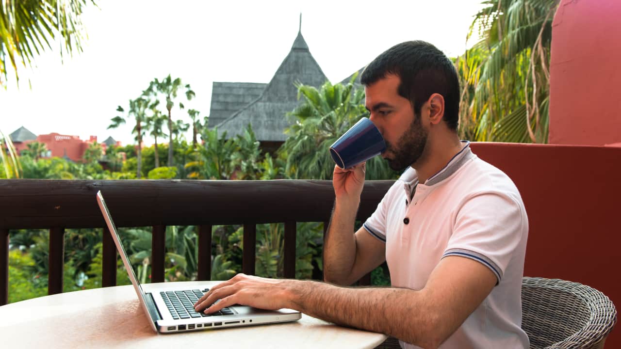 Man working with his laptop in a hotel terrace, he has a freedom to work from anywhere which is a benefit of nomadic lifestyle