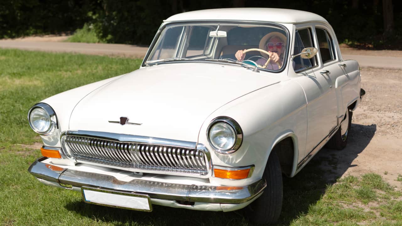 A traveler wearing sunglasses in a white classic car