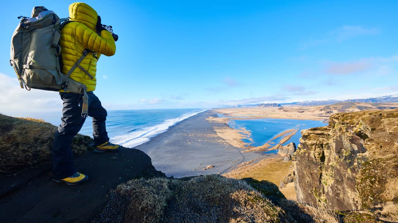 A man wearing yellow jacket standing on a rock and taking pictures