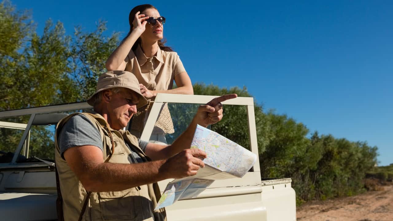 A woman is standing in a safari car while a man holding a map and pointing