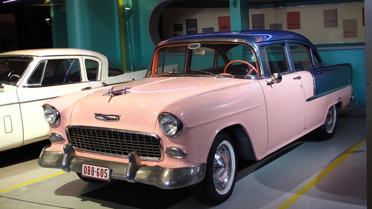 A pink Chevrolet Bel Air is displayed in a showroom, which is one of the classic convertible cars