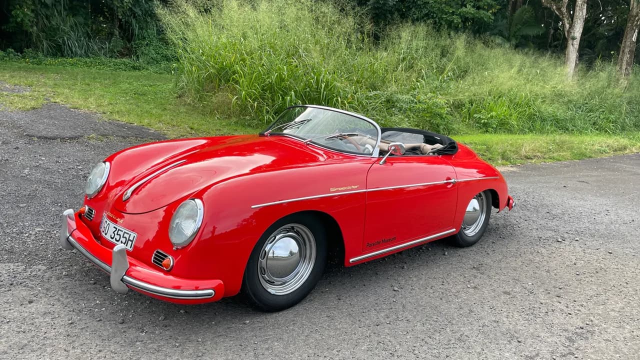 A 1956 Porsche 356 Speedster is parked on a wet road, with a grassy background