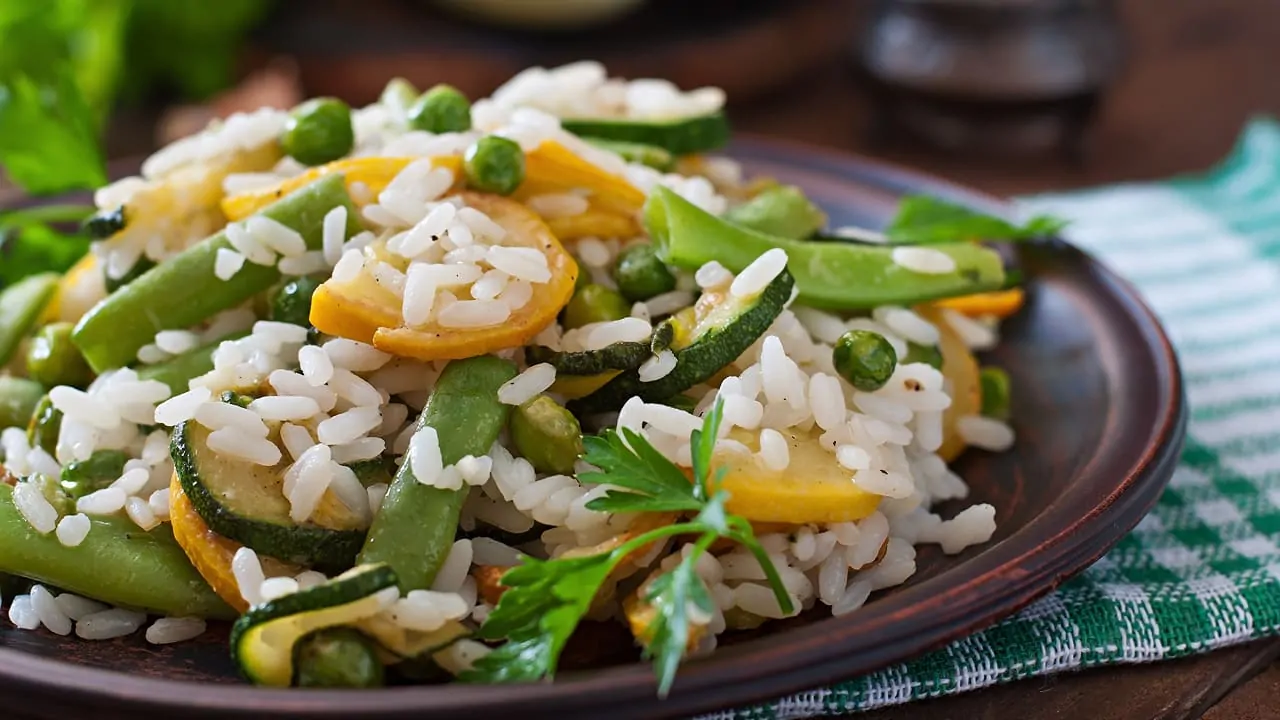 A plate filled with rice that includes zucchini and green peas