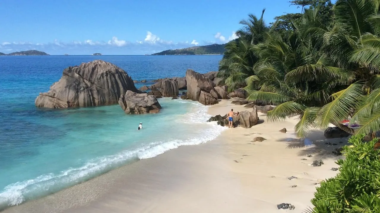 A big brown stone is in the middle of an African island, with many trees covering the view